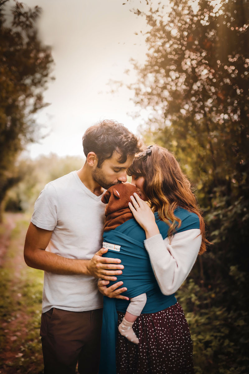 Couple qui porte bébé dans la meilleure écharpe de portage BASIC bleue de Love Radius en lui embrassant le front
